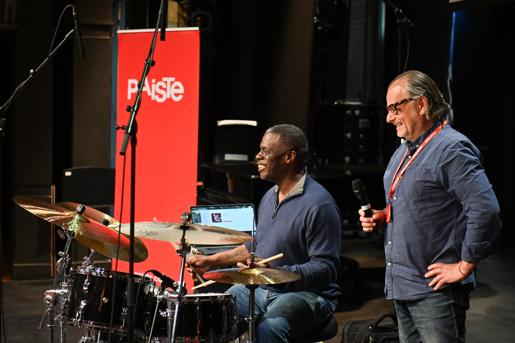 Two men leading a percussion event on stage, smiling.